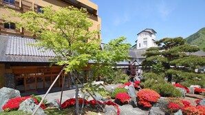 A traditional Japanese building with a tiled roof, surrounded by a garden with red and pink flowers, and a stone pathway.