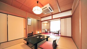 A traditional Japanese room with tatami flooring, a low table with cushions, sliding doors, and a view of the outside.