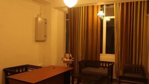 Ett hotellrum med ett skrivbord i trä, två stolar, ett litet bord, en lampa och ett fönster med gardiner.