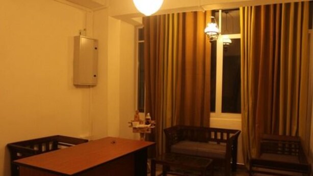 Hotellihuone, jossa on puinen työpöytä, kaksi tuolia, pieni pöytä, lamppu ja ikkuna, jossa on verhot.