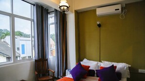 Ett hotellrum med ett stort fönster, en säng med vita och orange sängkläder och en trästol.