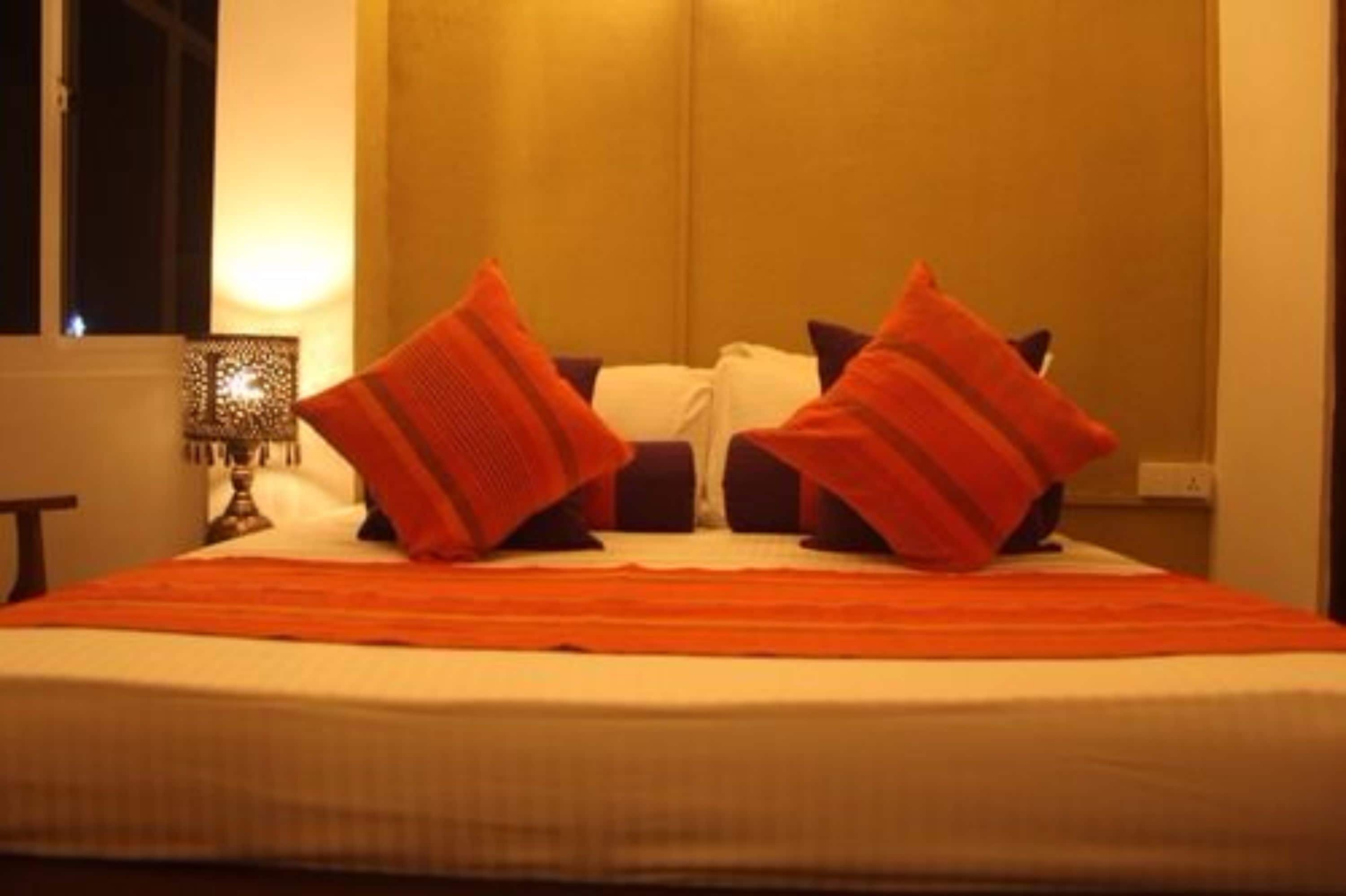 A neatly made bed with a striped orange bedspread and two red pillows.