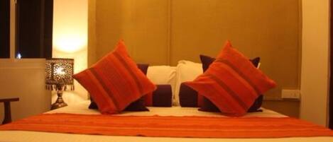 A neatly made bed with a striped orange bedspread and two red pillows.