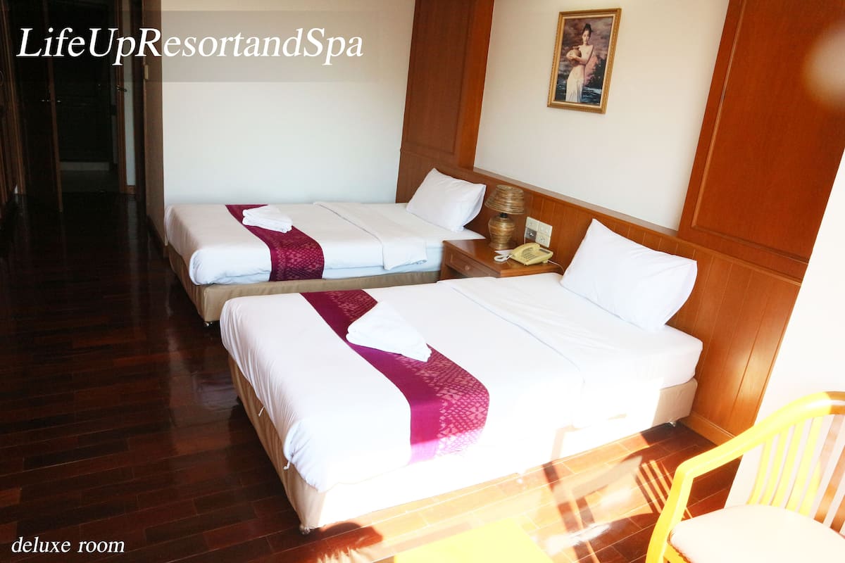 A deluxe room with two beds, wooden flooring, a bedside table with a lamp, and a chair.