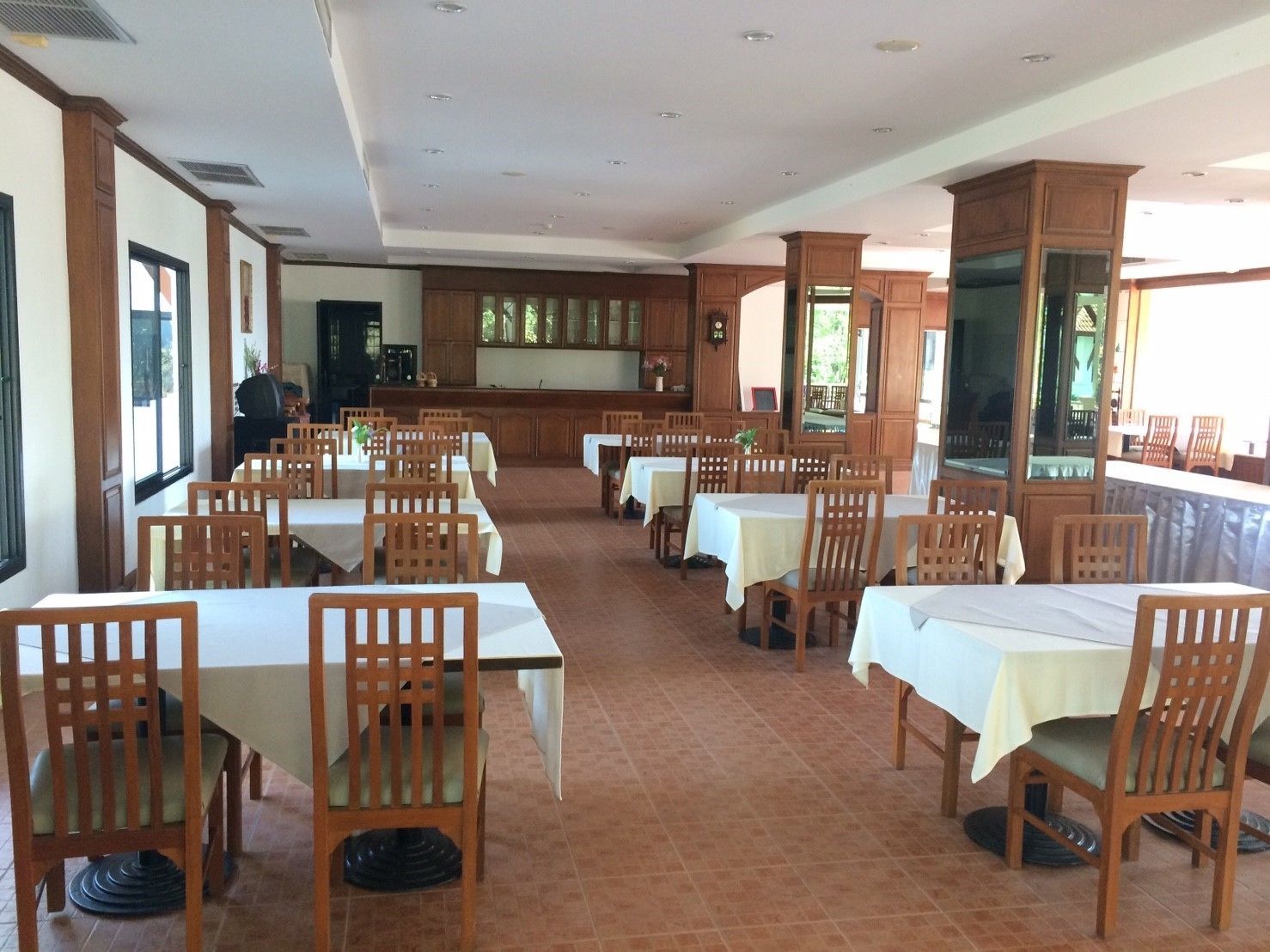 A spacious dining area with multiple tables and chairs, wooden cabinets, and large windows allowing natural light.