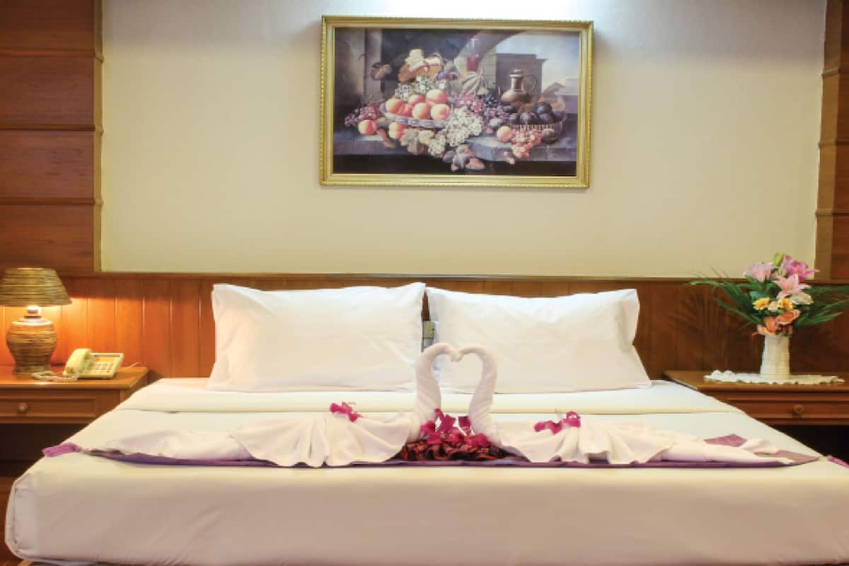 A hotel room with a neatly made bed, a painting on the wall, a nightstand with a lamp, and a vase of flowers.
