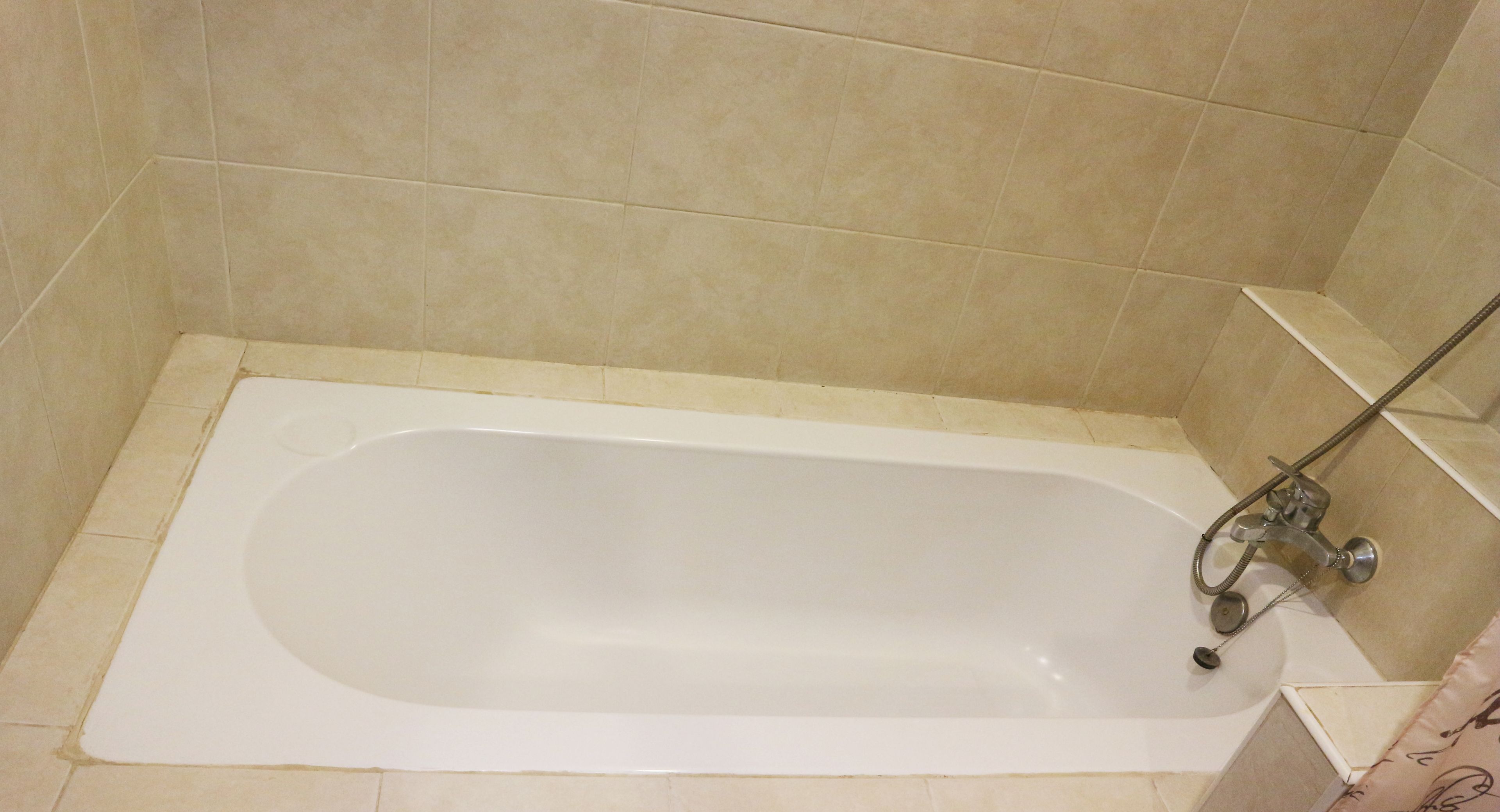 Una bañera estándar en un baño con azulejos color beige.