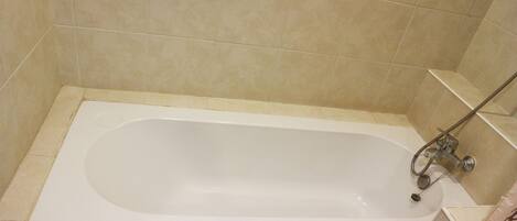 Una bañera estándar en un baño con azulejos color beige.
