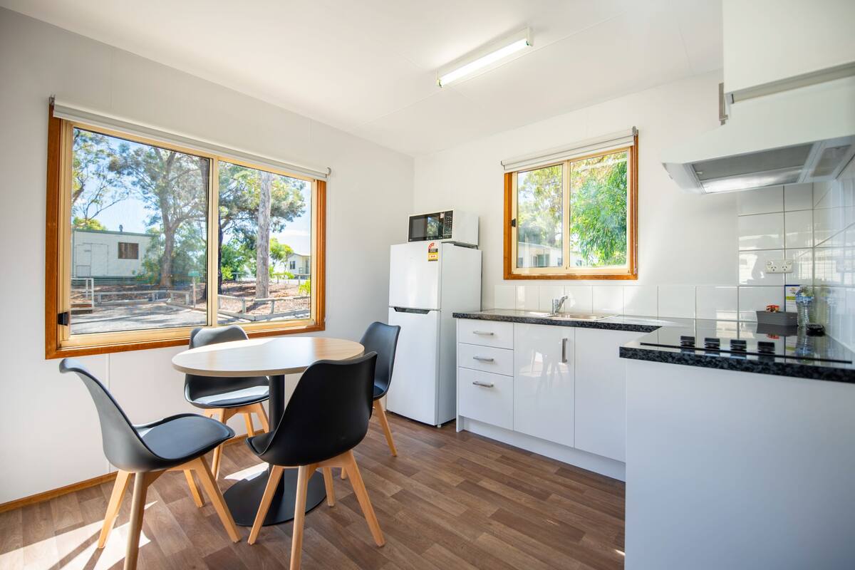 A modern kitchen with white cabinets, a black countertop, and a microwave on the fridge. There is a dining area with a round table and black chairs.
