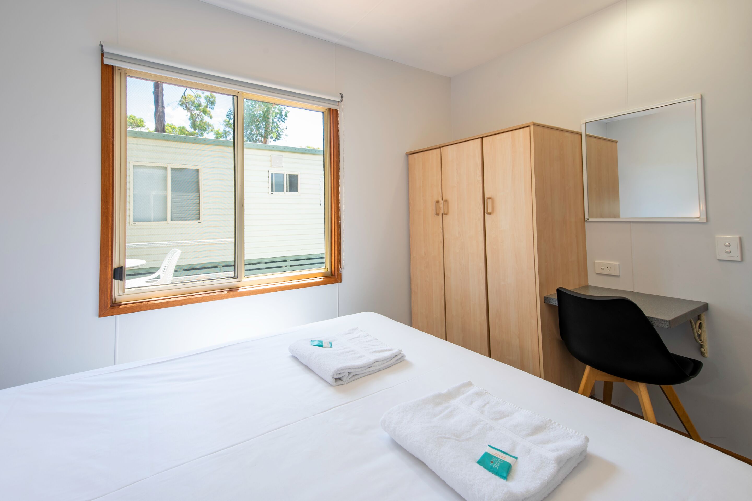 Quarto de hotel com cama, guarda-roupa de madeira, escrivaninha e cadeira.