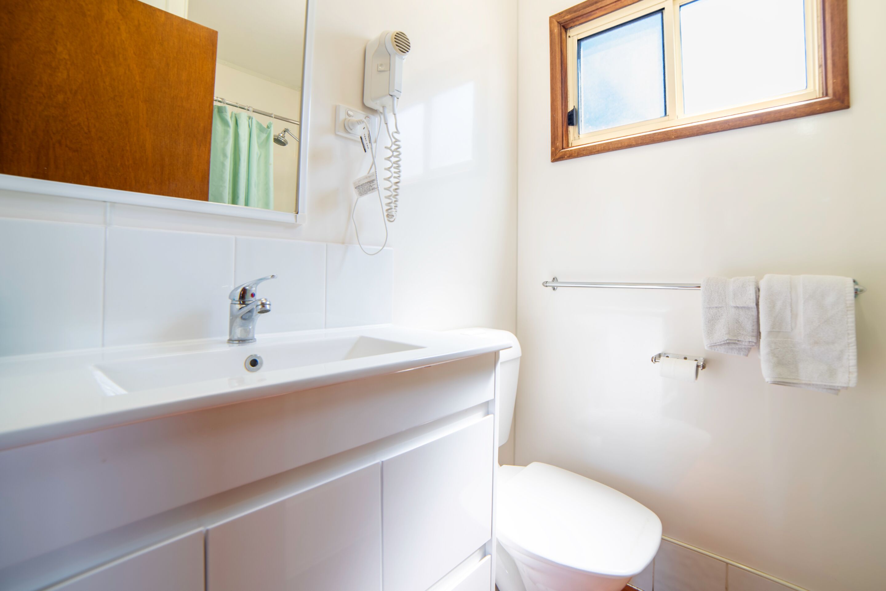 A bathroom with a white sink, a mirror, a hairdryer, a towel rack, and a window.