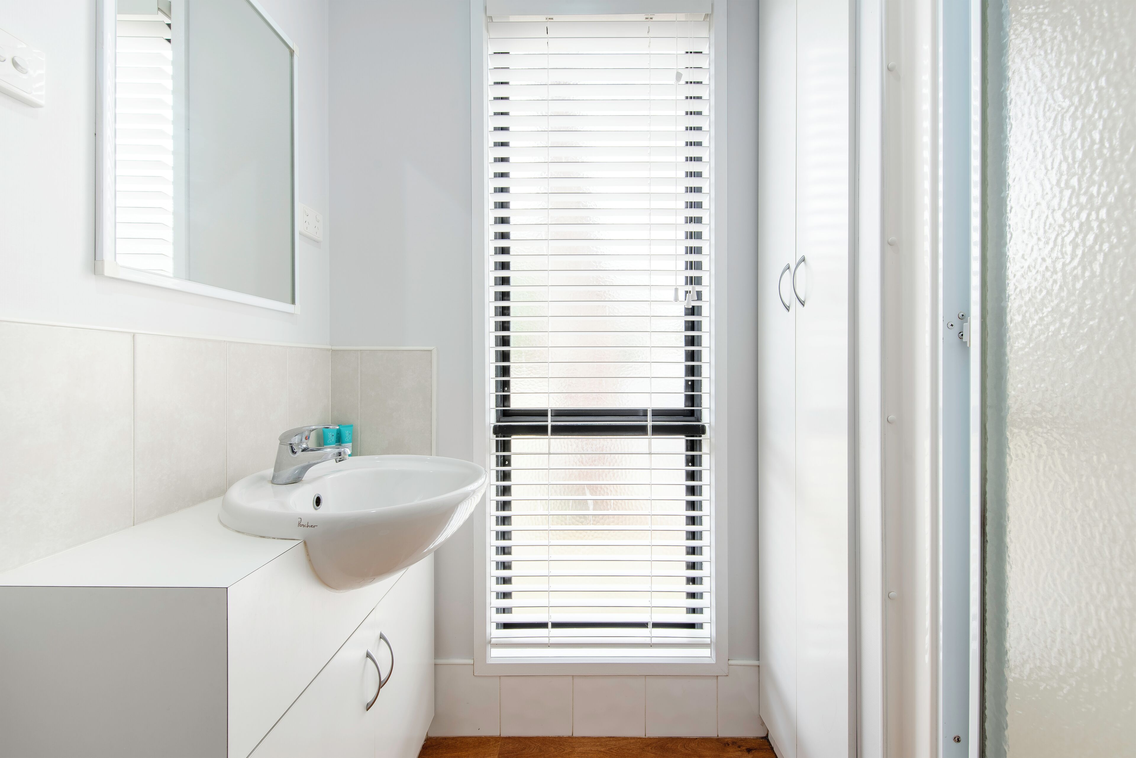 A bathroom with a white sink, mirror, and window with blinds.
