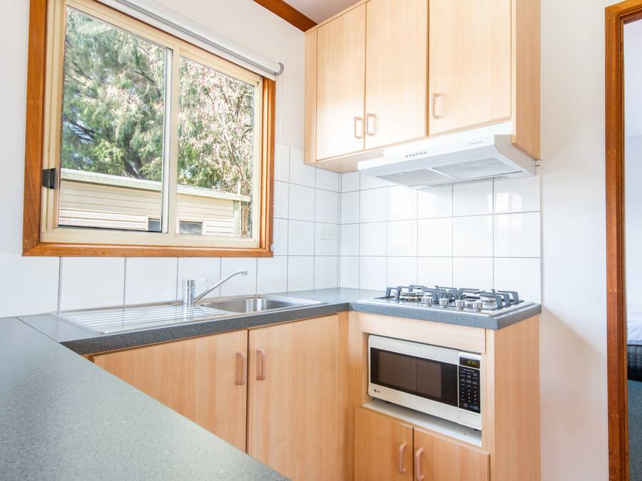A modern kitchen with wooden cabinets, a stainless steel sink, a built-in microwave, and a window with a view of trees.