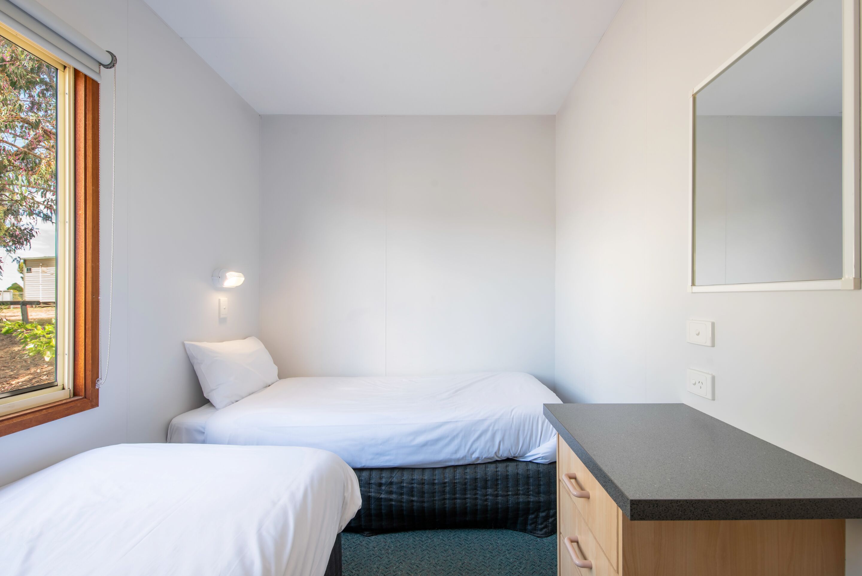 Un dormitorio pequeño y moderno con dos camas individuales, un aparador de madera y un espejo grande.