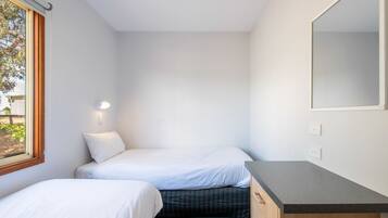 Un dormitorio pequeño y moderno con dos camas individuales, un aparador de madera y un espejo grande.
