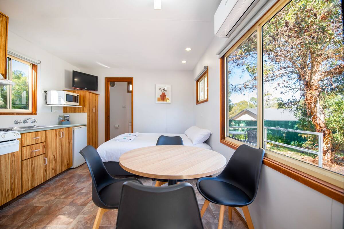 A modern kitchen with wooden cabinets, a microwave, and a dining area with a round table and four chairs.