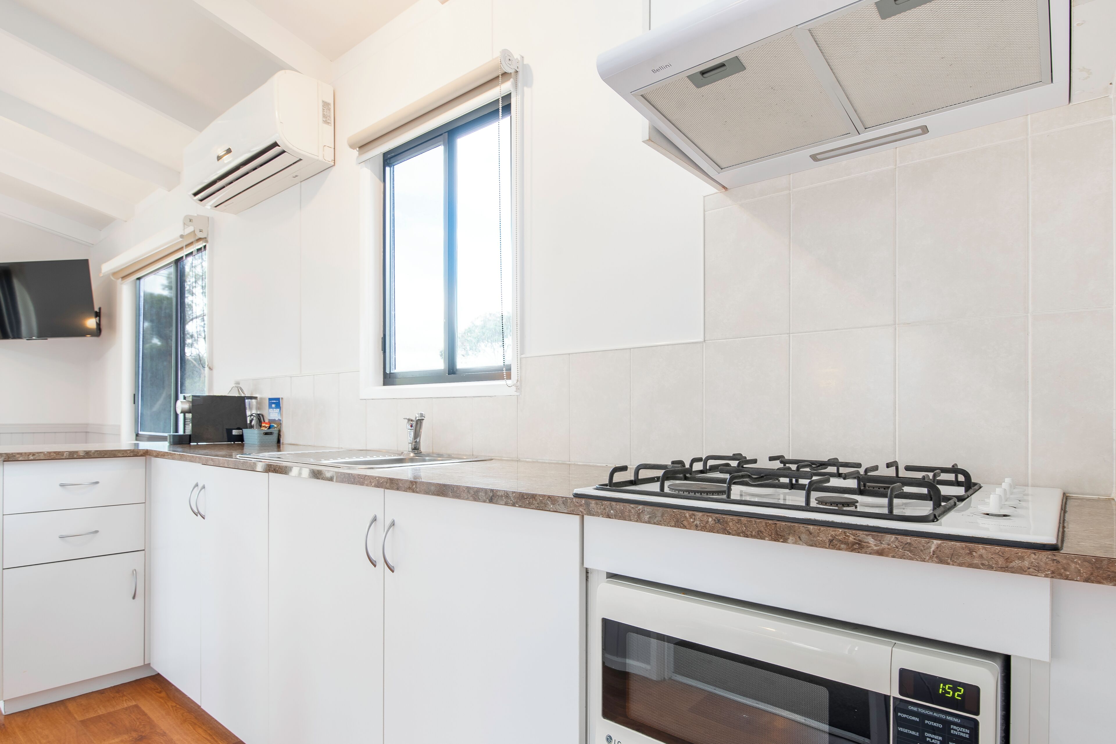 A modern kitchen with white cabinets, a gas stove, an oven, and a window with blinds.