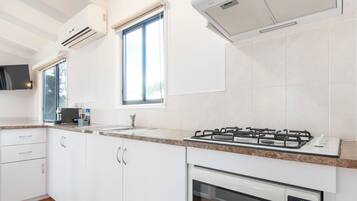 A modern kitchen with white cabinets, a gas stove, an oven, and a window with blinds.