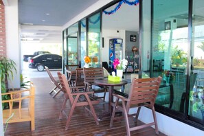 An outdoor seating area with wooden chairs and tables, a vending machine, and a view of the street. - Plus Hotel Loei (Wang Saphung)