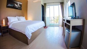 A hotel room with a bed, a desk, a TV, and a balcony with curtains.