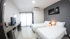 A hotel room with two beds, a desk with a computer, a chair, and a window with curtains.