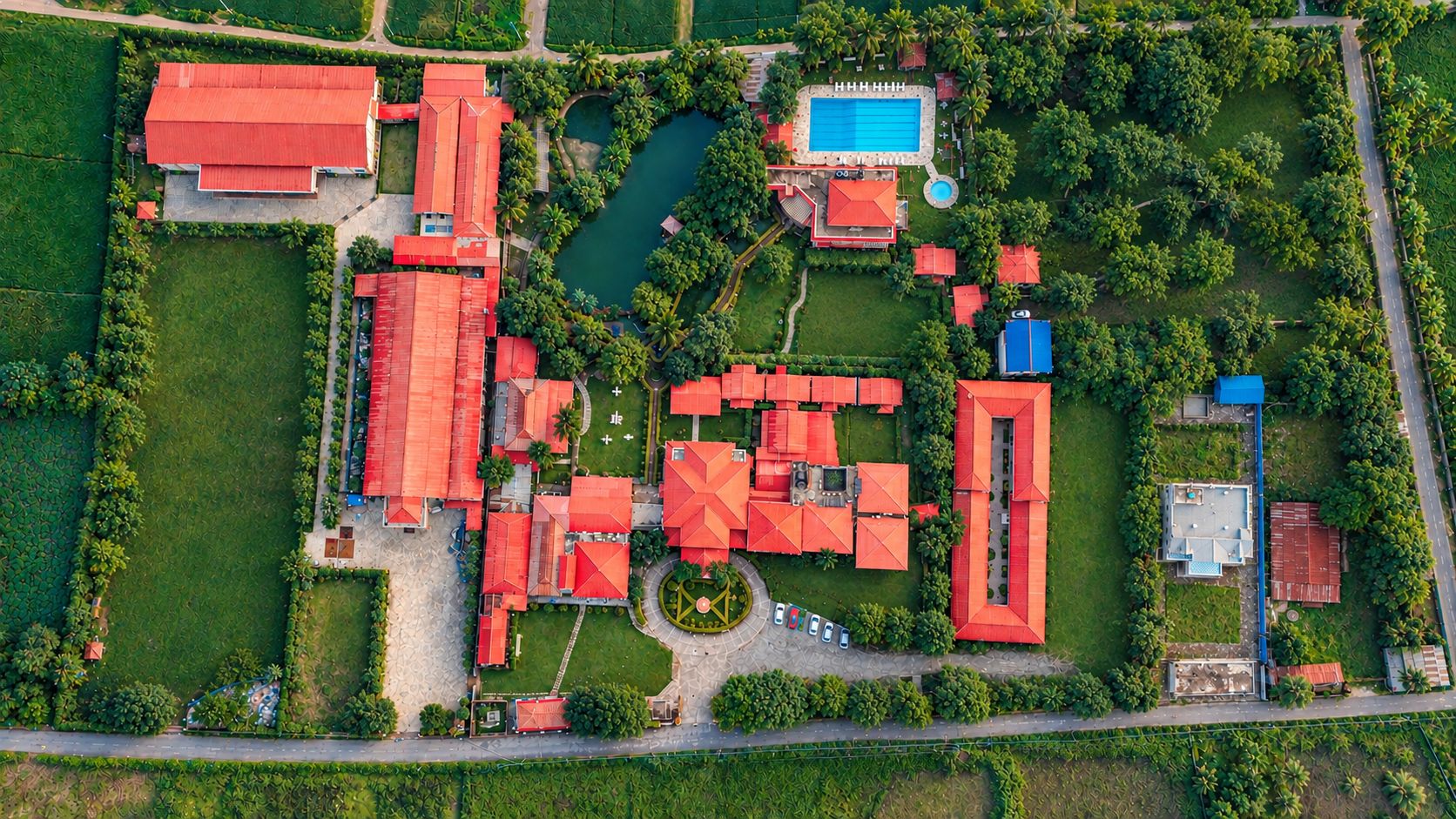 Vista aérea de una propiedad con varias edificaciones de tejados rojos, una piscina y vegetación circundante.