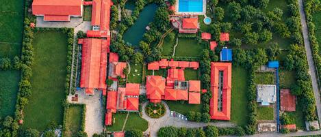 Vista aérea de una propiedad con varias edificaciones de tejados rojos, una piscina y vegetación circundante.