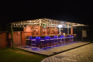 Zona de bar al aire libre con pared de ladrillo, varios taburetes y un área de estar cubierta.