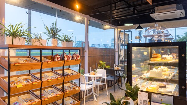 Una panadería con estantes llenos de productos horneados, una vitrina con pasteles y áreas de estar.