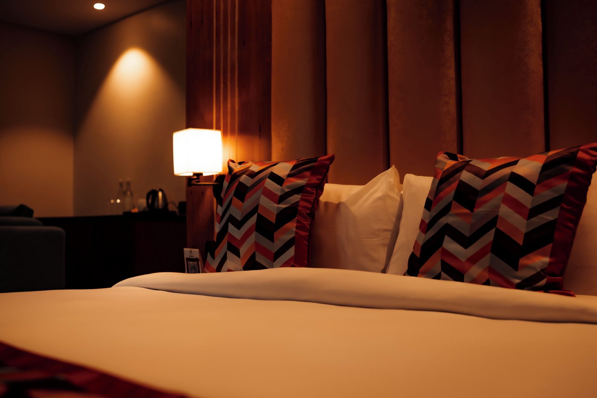A hotel room with a bed, a nightstand, a lamp, and a window with curtains.
