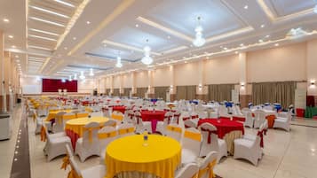 Un salón de banquetes con mesas redondas y sillas blancas, algunas con cintas amarillas.
