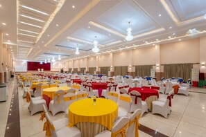 Un salón de banquetes con mesas redondas y sillas blancas, algunas con cintas amarillas.