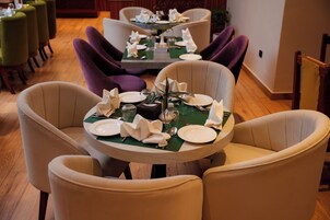 Comedor con mesas redondas dispuestas para cuatro personas, rodeado de sillas de diversos colores.