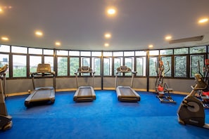 Une salle de sport équipée de tapis de course, de vélos elliptiques et de vélos d’exercice, avec de grandes fenêtres et un tapis bleu.