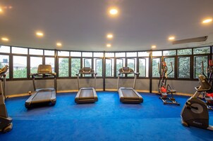 Un gimnasio con cintas de correr, elípticas y bicicletas estáticas, ventanas amplias y una alfombra azul.