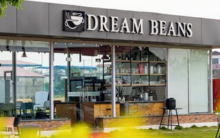 Una cafetería llamada 'Dream Beans' con un mostrador visible, zona de estar y vistas del entorno.