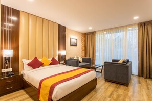 Una habitación de hotel con una cama grande, dos sillones, una mesita y un escritorio con una lámpara.
