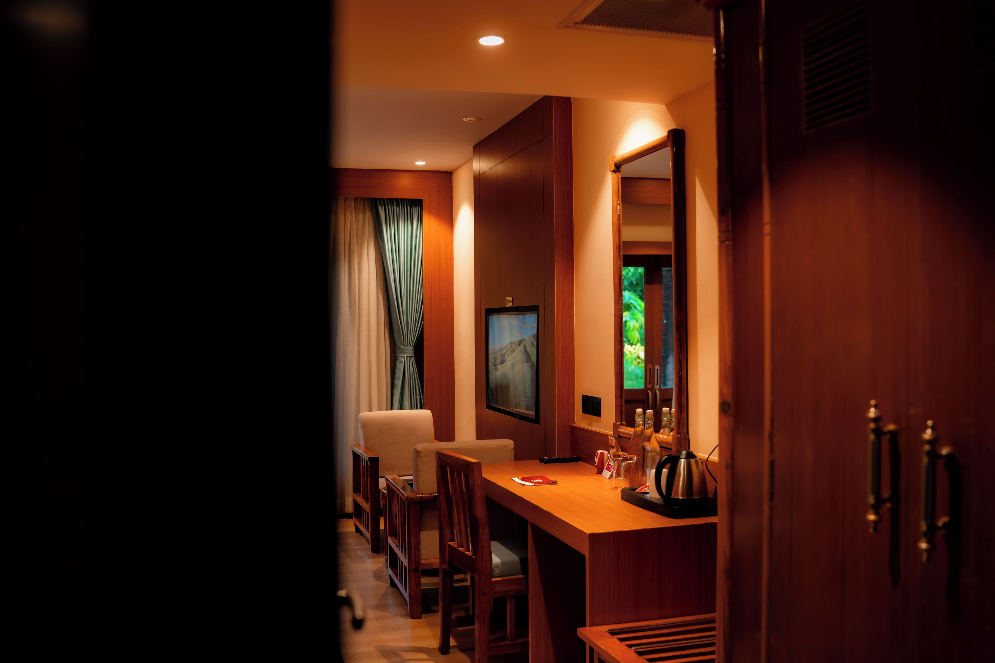 A hotel room with a wooden desk, a chair, a television, and a window with curtains.