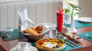 Desayuno con un plato de huevos, tostadas y una bebida roja, una cesta de bollería y un florero con plantas.
