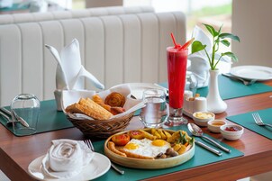A breakfast setting with a plate of eggs, toast, and a red drink, a basket of pastries, and a vase of greenery.