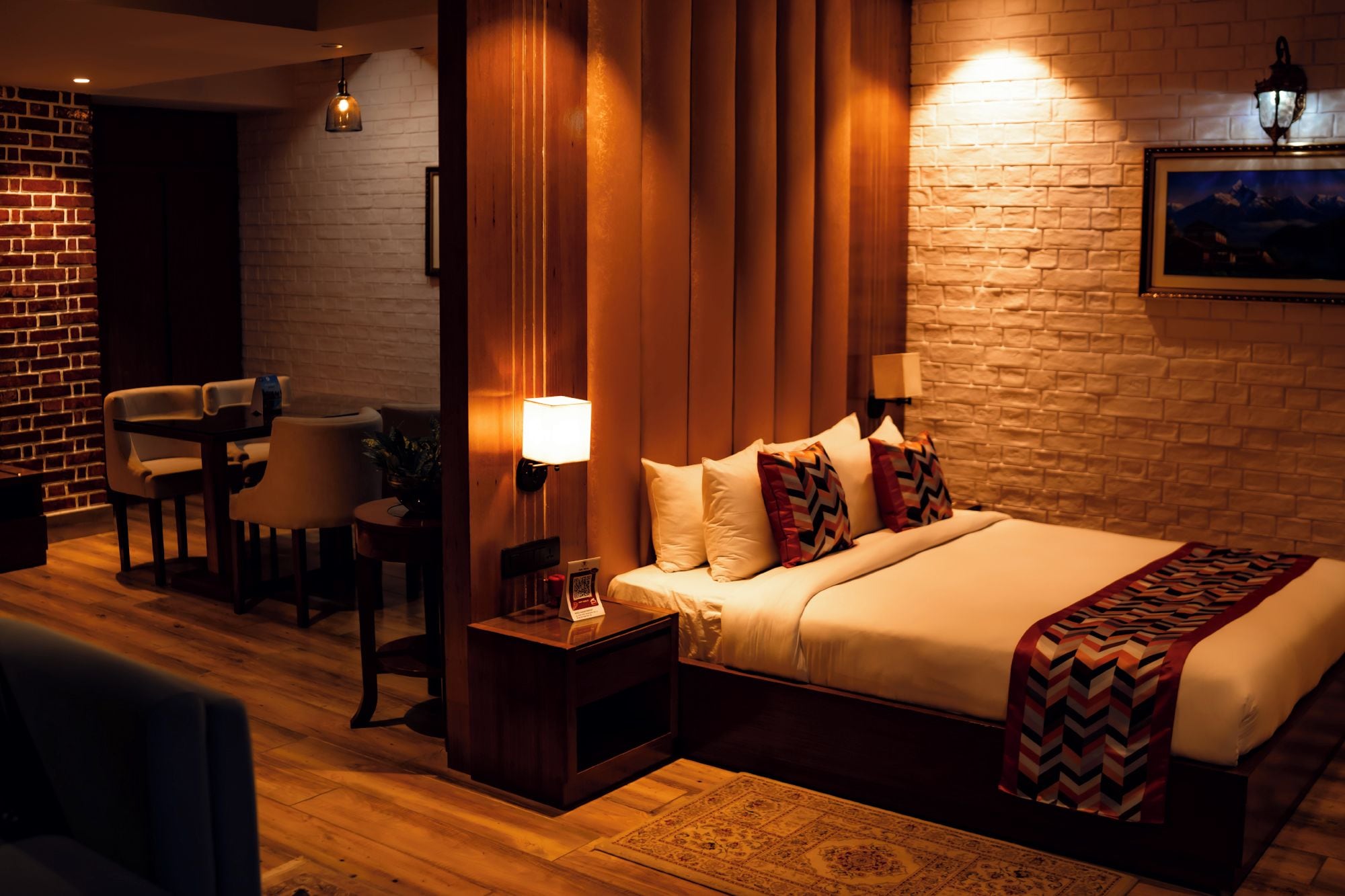 A hotel room with a bed, bedside table, lamp, and a seating area with chairs.