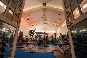 Un gimnasio con diversos equipos de ejercicio, espejos y ventiladores de techo.