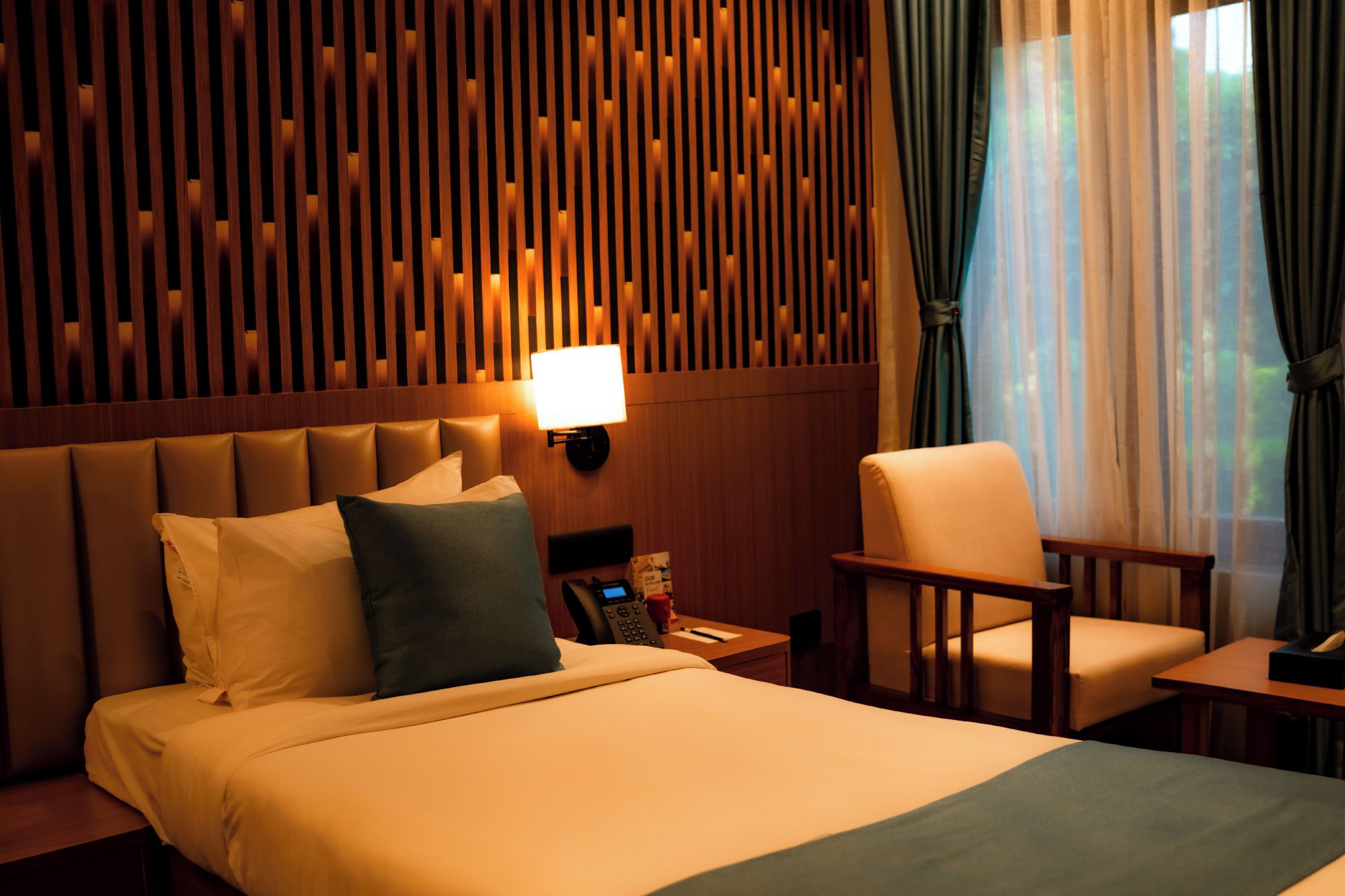 Camera d'albergo con un letto grande, un comodino, una sedia, una lampada e un pannello di legno a parete.