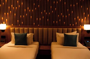 Habitación de hotel con dos camas, cabecero de madera con listones y lámparas de noche.