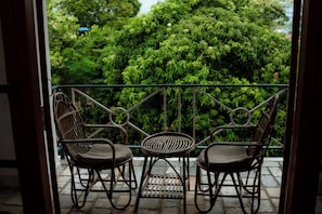 Varanda com duas cadeiras de vime e uma pequena mesa, com vista para um jardim verdejante.