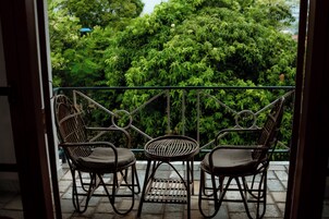 Un balcón con dos sillones de mimbre y una mesita, con vistas a un exuberante jardín verde.