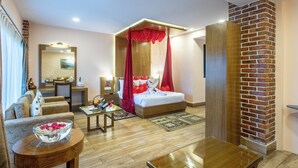 Habitación de hotel con cama, zona de estar con sofá y sillones, mesa de comedor y pared decorativa de ladrillo.