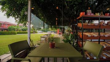 An outdoor seating area with tables and chairs, a potted plant, and a display of baked goods.