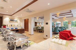 A hotel dining area with buffet service, a painting on the wall, and a view of the outdoors.