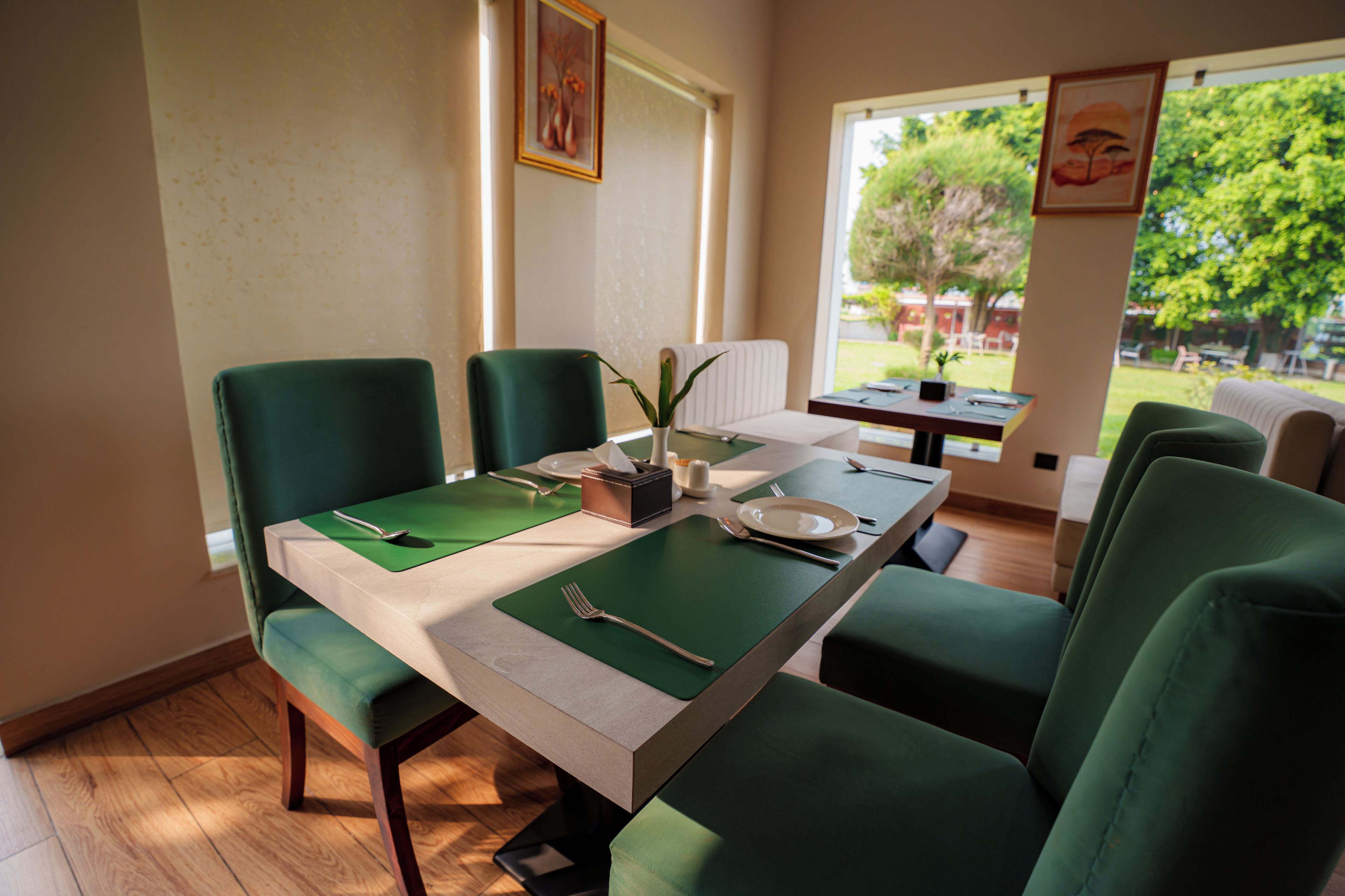Comedor con una mesa dispuesta para cuatro, sillas tapizadas en verde y ventana con vistas al follaje exterior.